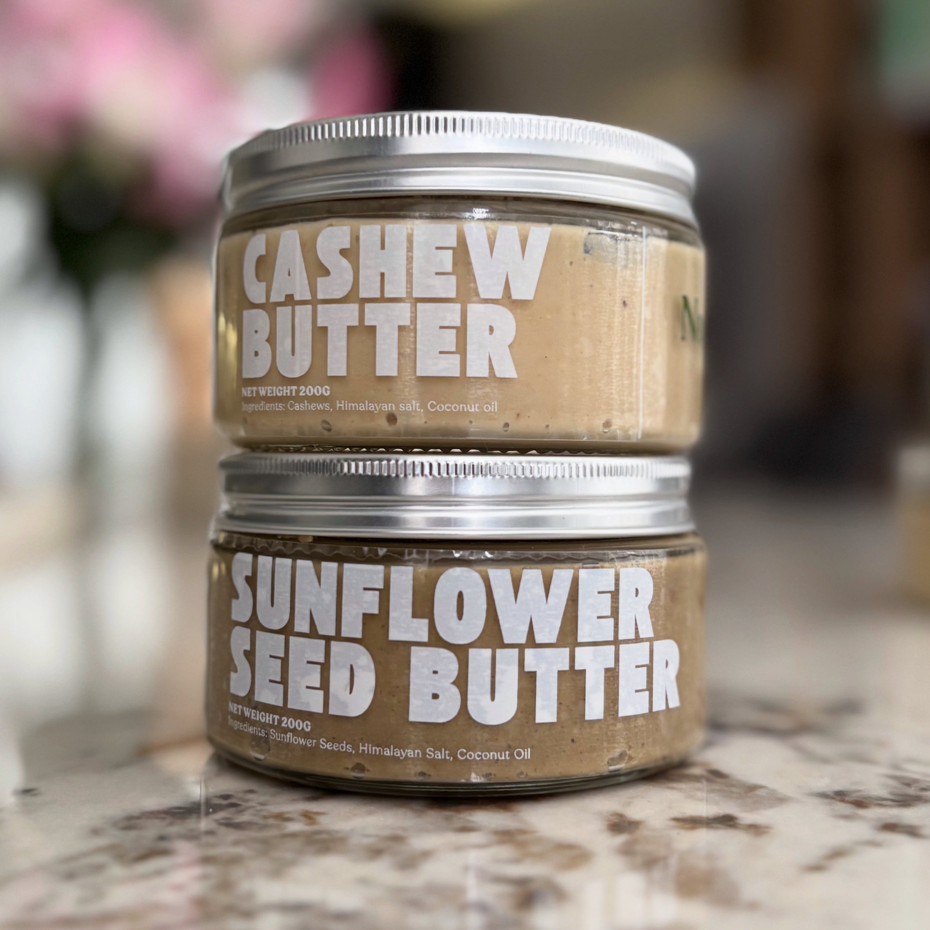 Two jars of cashew and sunflower seed butter on a marble surface. sunflower seed butter by NuttaNut. selai biji matahari di indonesia. jakarta, surabaya, cirebon same day delivery. healthy nut butter NuttaNut